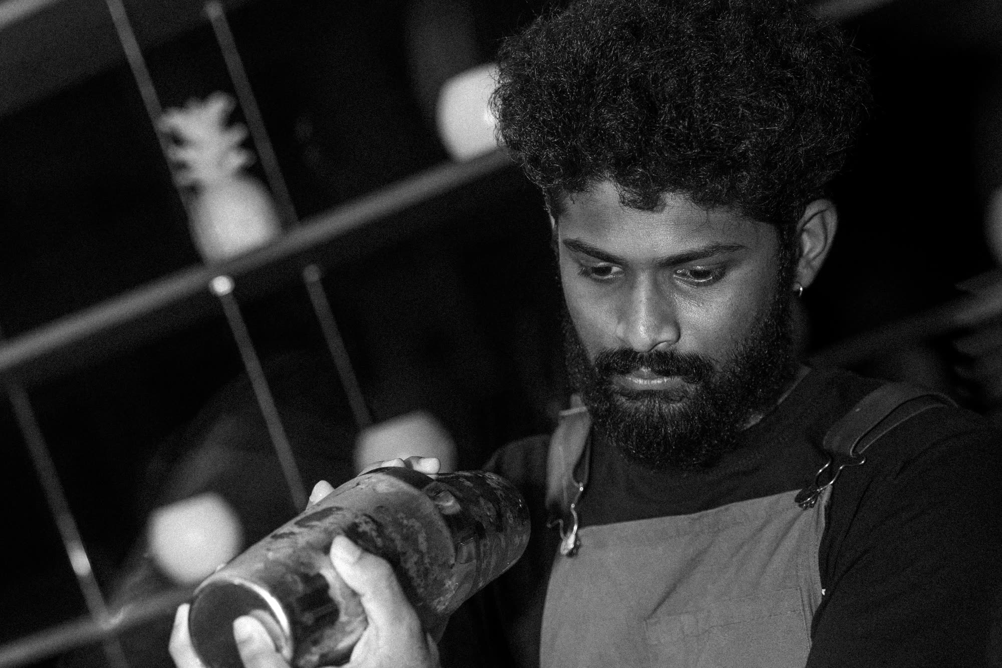 A bartender in an apron shaking a cocktail at the back bar; black and white