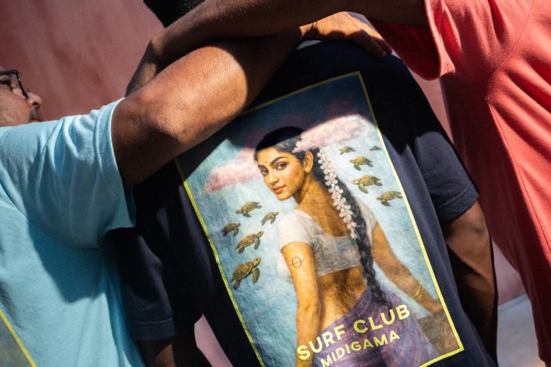 Three friends arm in arm seen from behind, the middle one in a navy Surf Club Midigama tee printed with an illustrated portrait