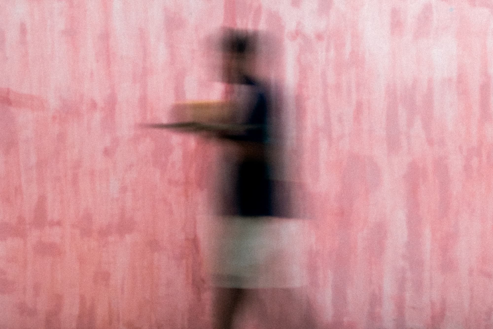 A member of the team, blurred by movement, carrying a tray past a pink plaster wall